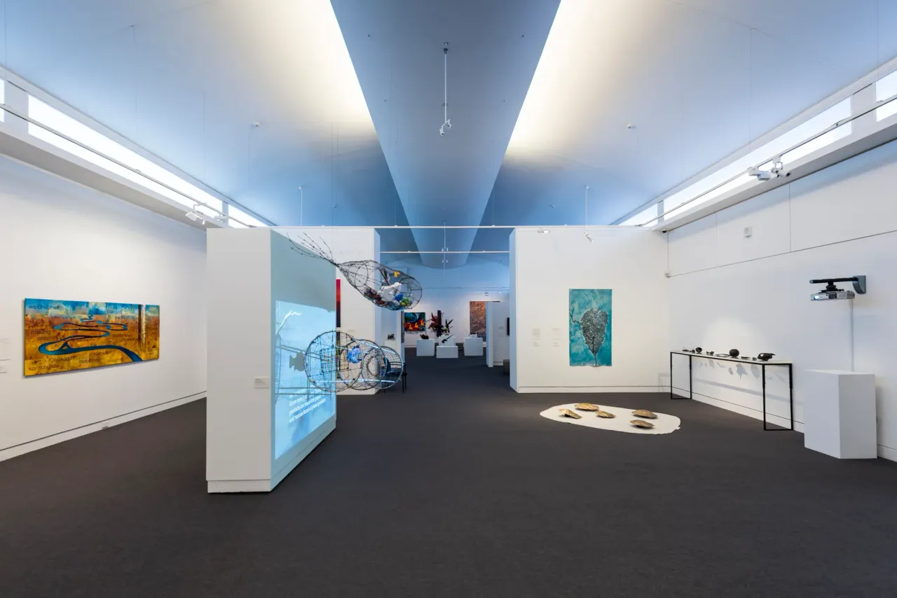White-walled exhibition space at Mornington Peninsula Regional Gallery with paintings, wire fish sculptures and a floor installation