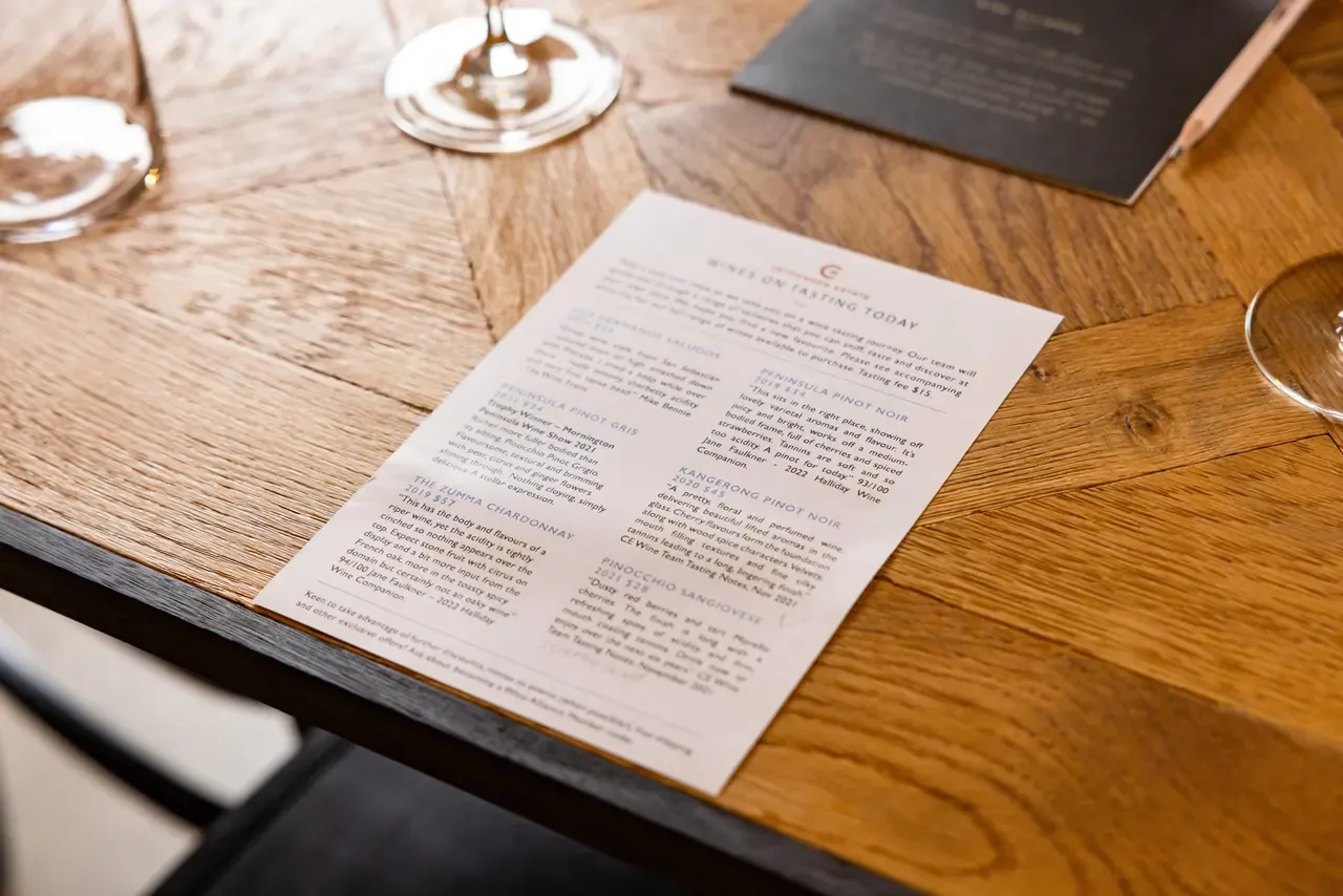 Crittenden Estate tasting sheet listing the wines on pour today, lying on a timber table beside empty wine glasses
