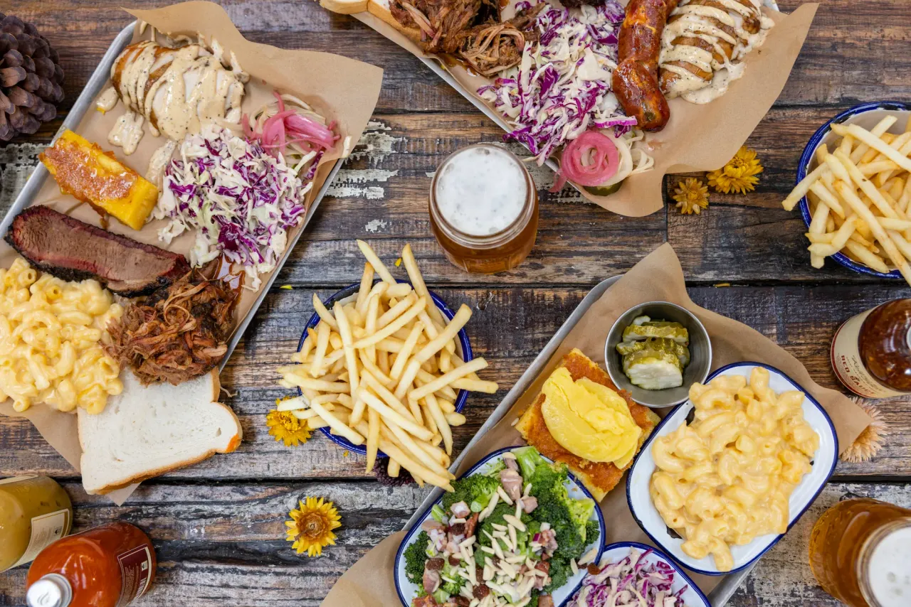 Overhead spread of brisket, pulled pork, sausage, mac and cheese, chips, coleslaw and beer on a timber table
