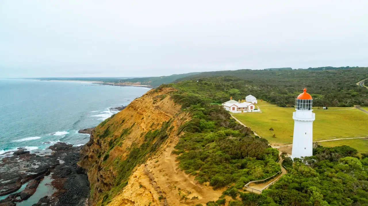 Aerial view of the white Cape Schanck lighthouse and keepers' cottages on a clifftop above a rocky coastline