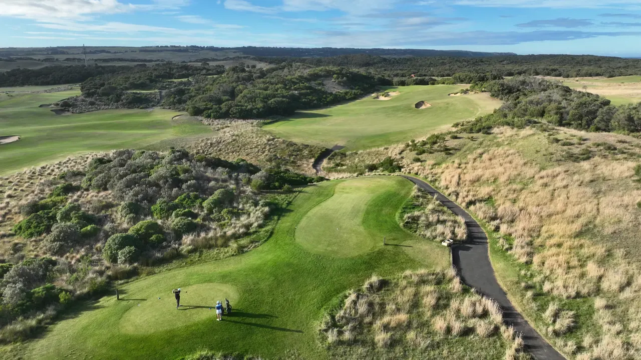 Aerial view over St Andrews Beach Golf Course, with golfers on a tee, a cart path winding through dune grass and fairways beyond