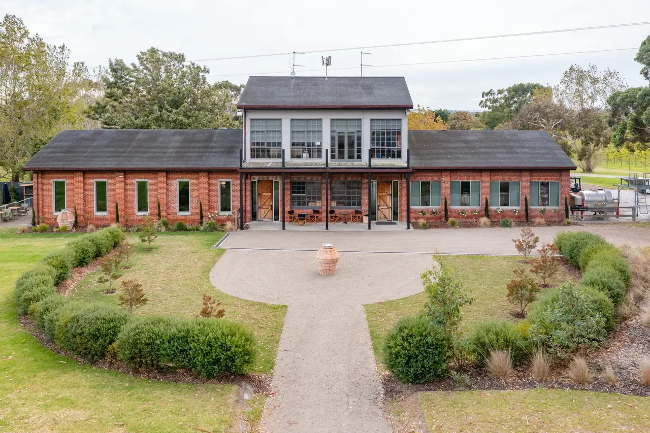 Red-brick Trofeo Estate building with a glazed upper storey, circular gravel drive and hedged garden beds in front