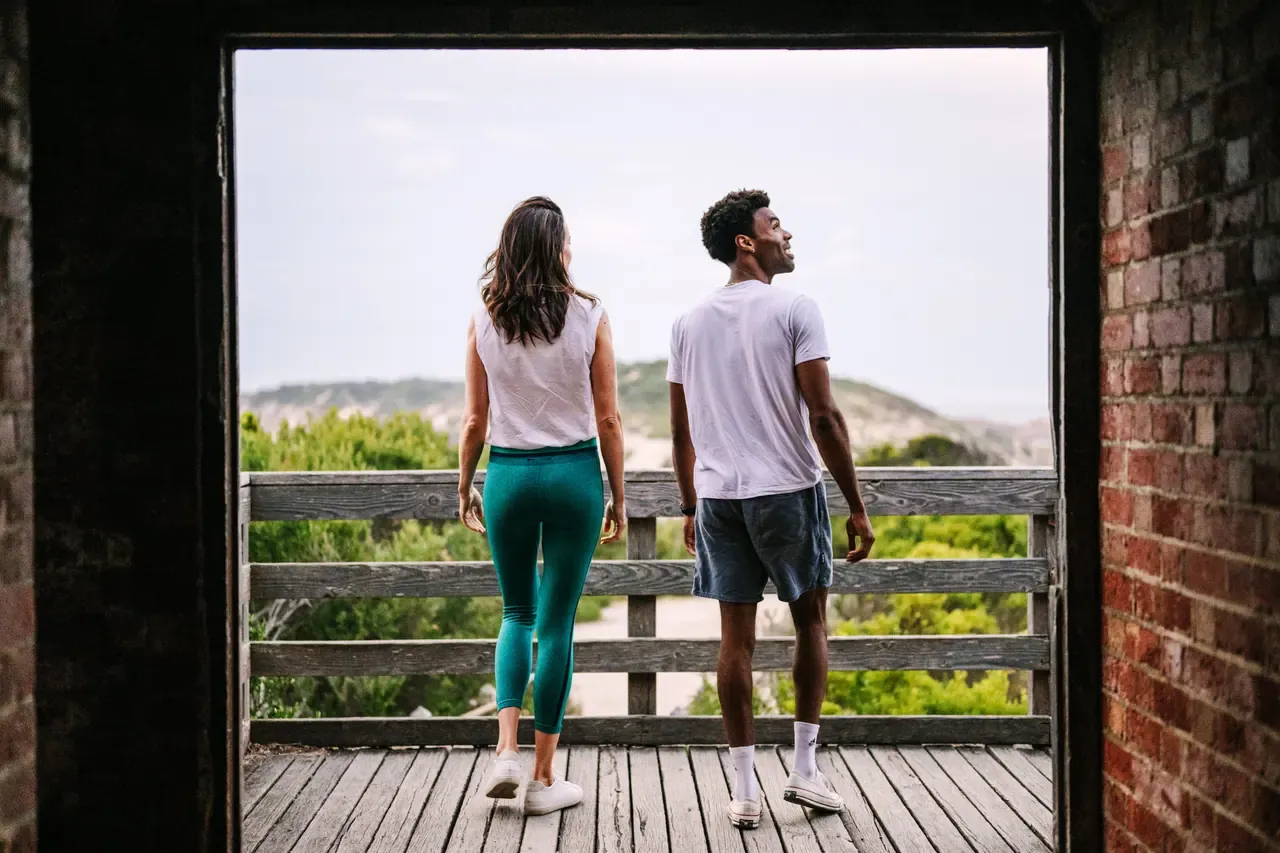 Two people stand on a timber deck framed by a brick doorway at Point Nepean, looking out over coastal scrub and hills