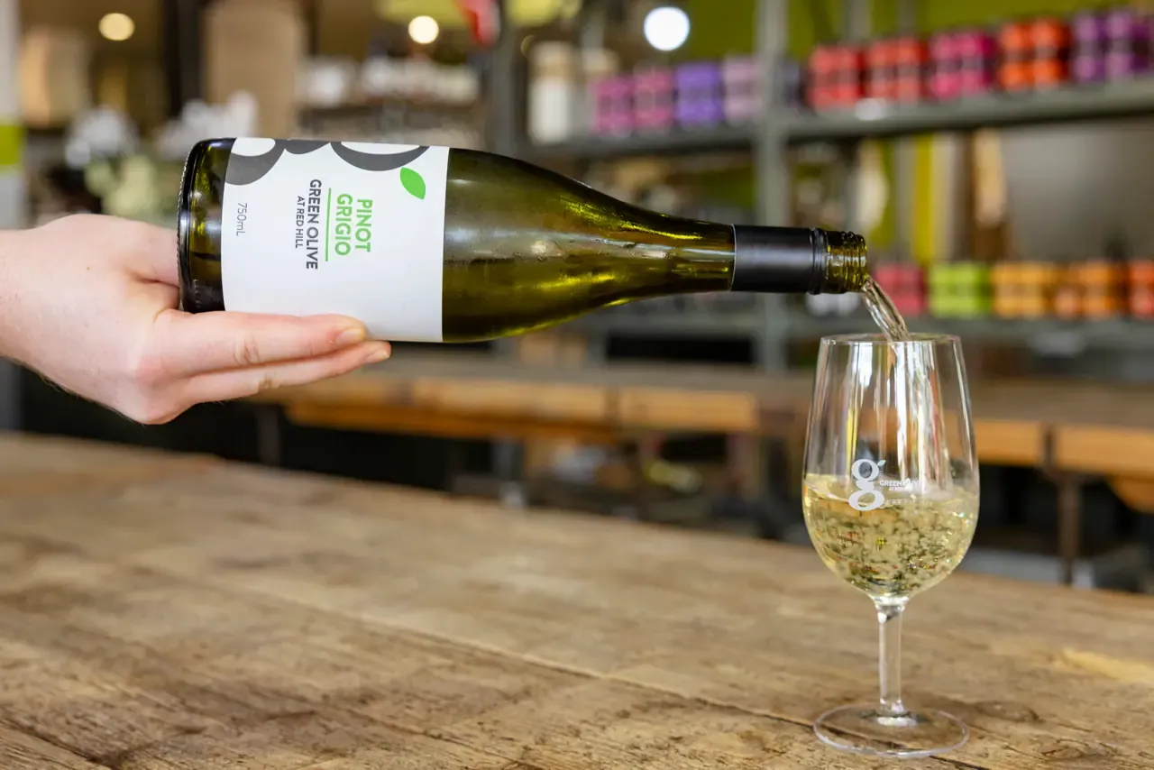 A bottle of Green Olive at Red Hill Pinot Grigio being poured into a tasting glass on a timber bench