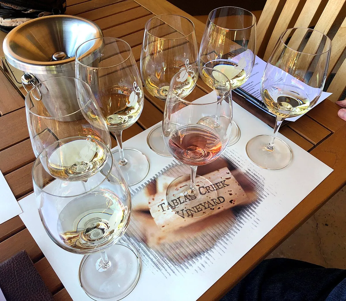 White wine tasting flight at a vineyard cellar door, chardonnay in stemware against a winery backdrop