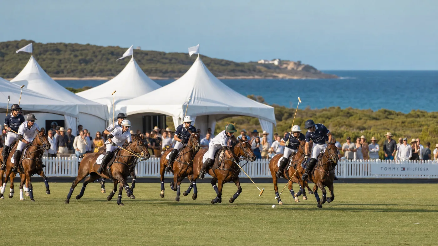 Polo players on horseback mid-match at Portsea Polo, with white marquees and the coastal foreshore behind them