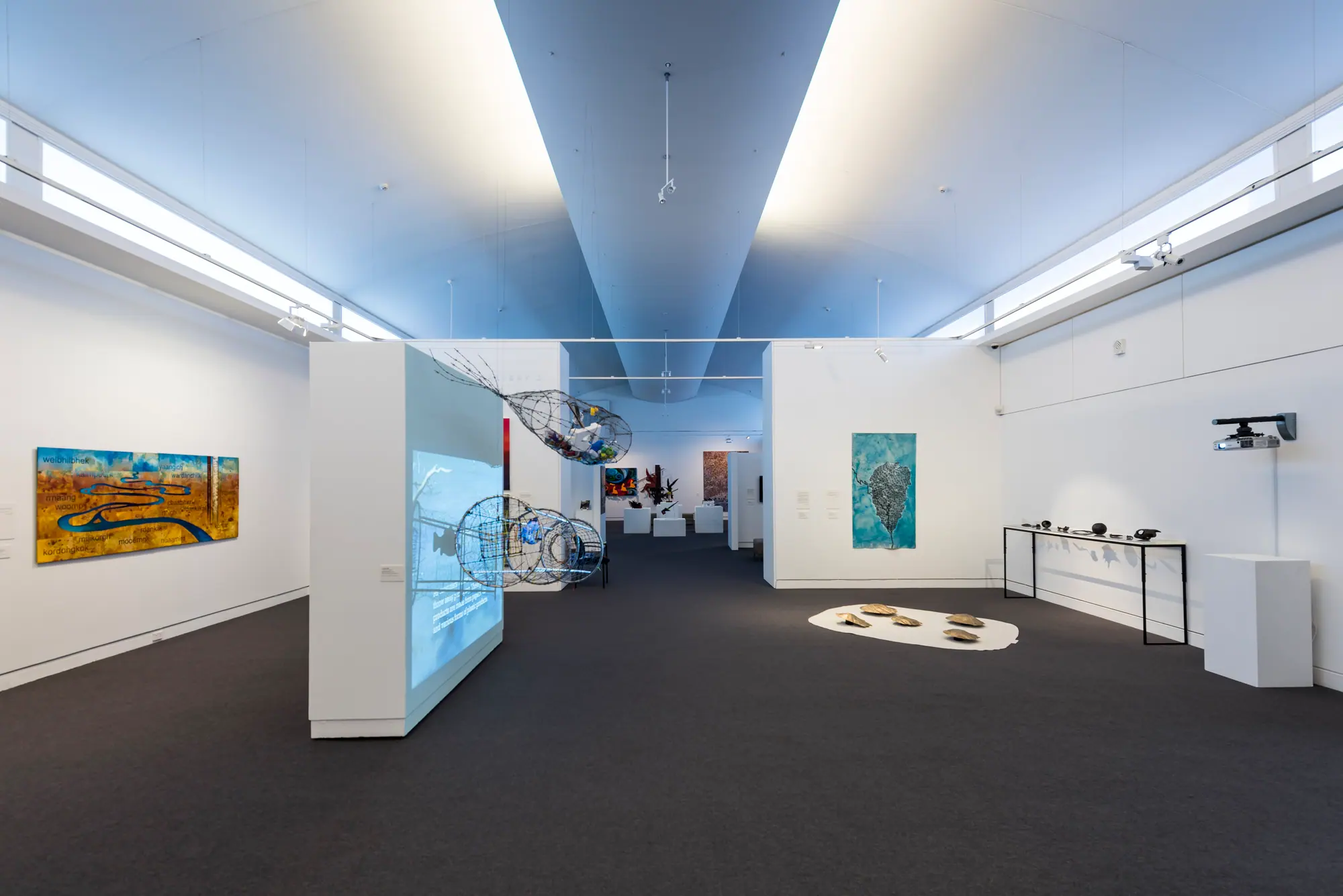 White-walled exhibition space at Mornington Peninsula Regional Gallery with paintings, wire fish sculptures and a floor installation