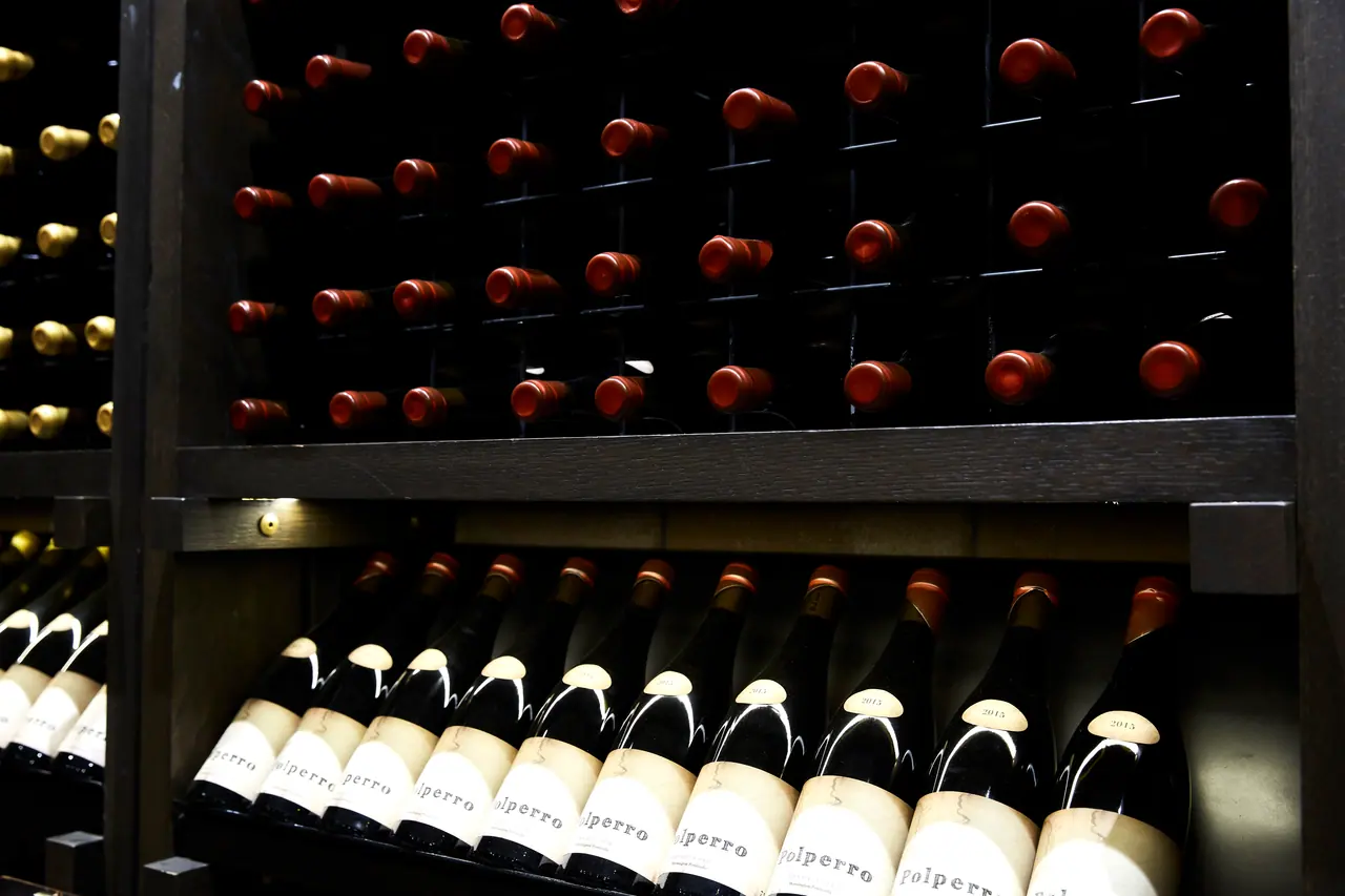Rows of wine bottles stored in dark timber racks in the cellar at Polperro Winery, with labelled bottles on the lower shelf