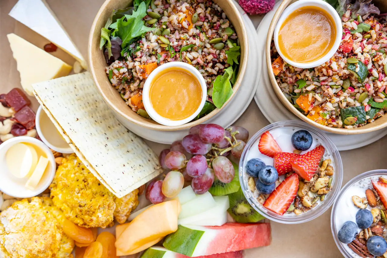 Overhead view of a shared platter with grain salads, cheese, crispbread, fresh fruit and berry yoghurt cups at Peninsula Hot Springs