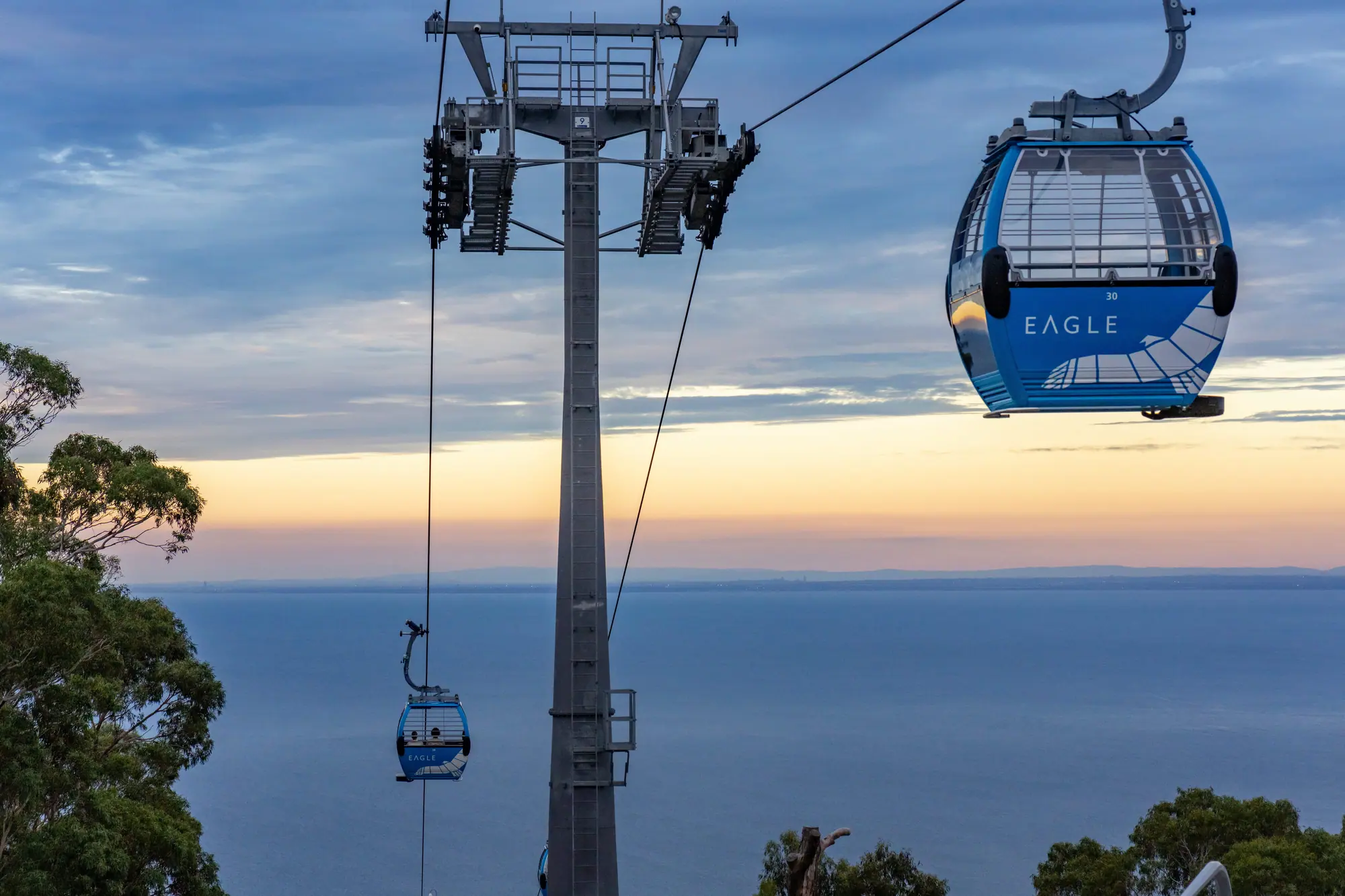 Arthurs Seat Eagle gondolas pass a support tower above the bay as a pale band of light sits on the horizon