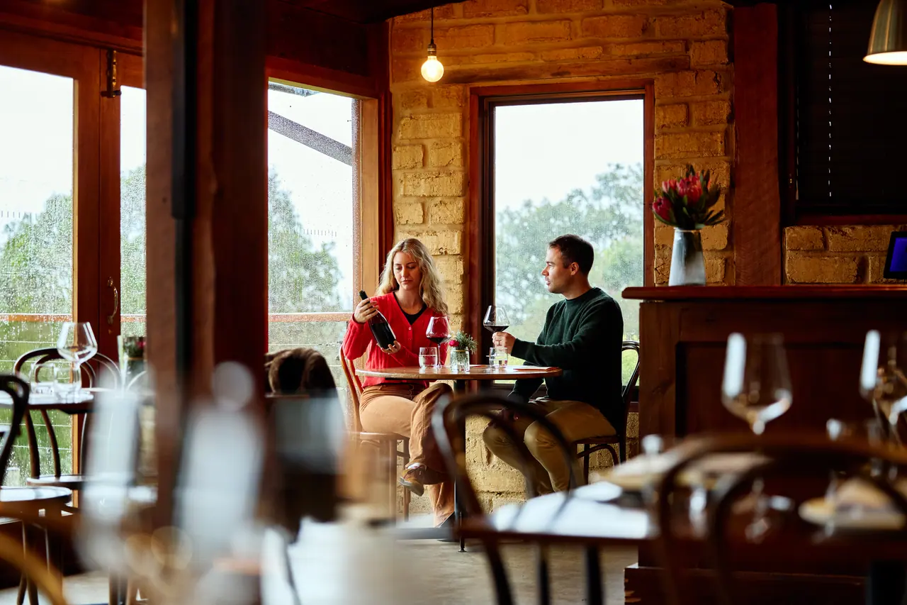 Two guests at a small table sharing a bottle of red wine in the mudbrick cellar door at Avani Winery
